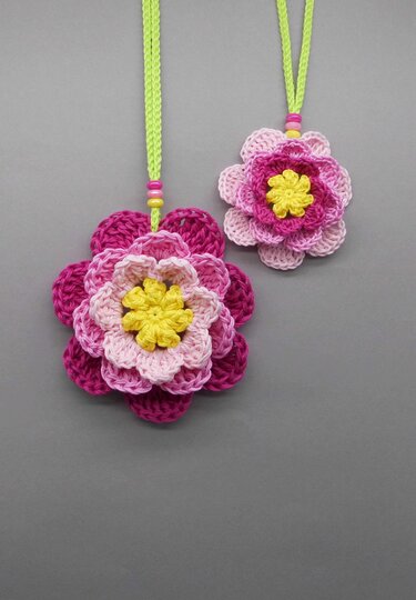 Two crocheted pink and yellow flowers hanging from bright green cords with beads.