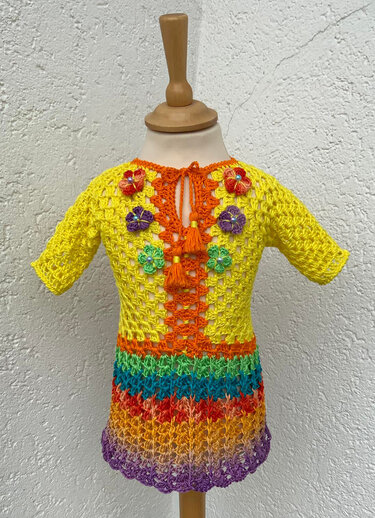 Gehäkeltes Kinderkleid mit gelbem Oberteil, orangefarbener Frontblende, kleinen Blumen und buntem Streifenrock auf einer Schneiderpuppe