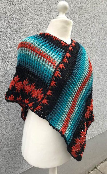 Häkelponcho mit luftigem Gittermuster, diagonalen Farbblöcken in Türkis/Blau, schwarzen Streifen und sternförmigen Reliefstichen am Rand.