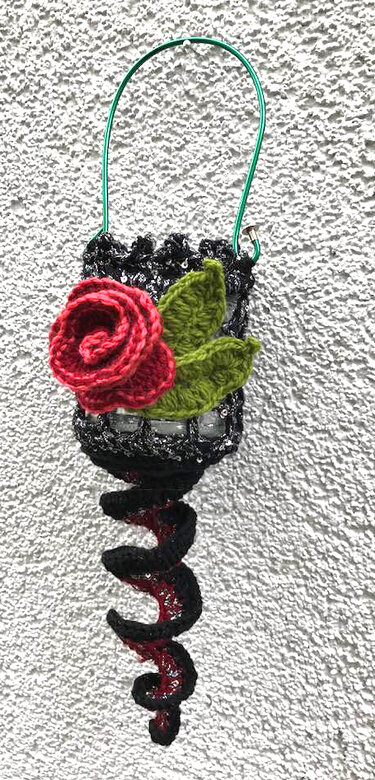 Kleiner gehäkelter Wandhänger mit roter Rose, grünen Blättern und gedrehter Spirale an grünem Drahtbügel