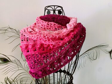Dreieckiger gehäkelter Loop in Rosa- und Pinkverlauf mit offenen Maschen auf einer Metall-Schneiderbüste