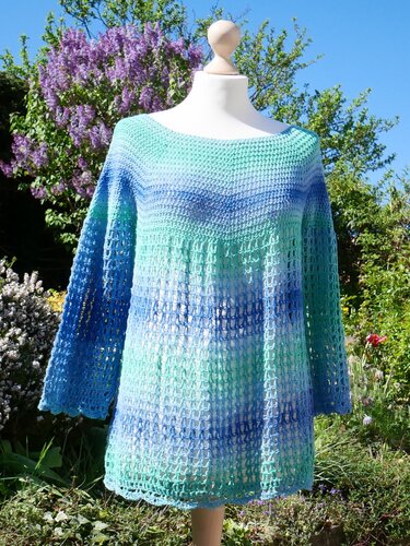 Türkis-blaue Häkel-Tunika mit dichtem Oberteil und offenem Netzmuster auf Schneiderbüste im Garten
