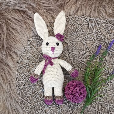 White crocheted amigurumi bunny with purple trim beside lavender sprig
