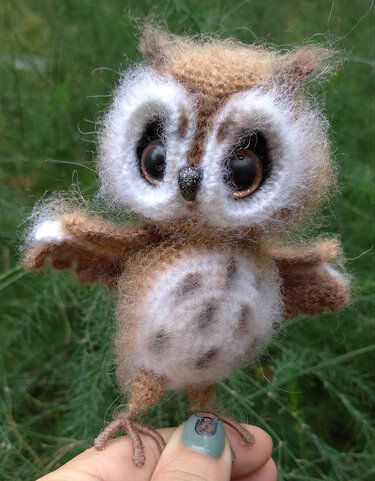 kleine gehäkelte braune Amigurumi-Eule mit großen Augen, gehalten an den Krallen