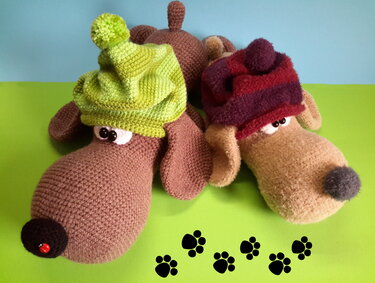 Zwei gehäkelte Amigurumi‑Hunde mit bunten Mützen auf grünem Hintergrund