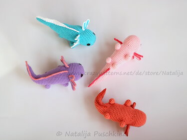 four crocheted amigurumi axolotls in turquoise, pink, purple and coral on white background