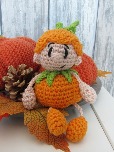 Handgehäkeltes Kürbis-Amigurumi mit grünem Blattkragen, orangefarbenem Körper und aufgesticktem Gesicht
