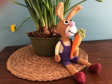 Gehäkelter Amigurumi-Hase mit langen Ohren, violetter Latzhose und Karotte