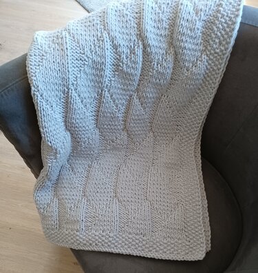 Cremefarbene, grob gestrickte Decke mit Rautenmuster auf grauem Sessel