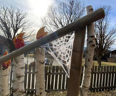 Weißes gehäkeltes Spinnennetz an Holzrahmen vor Birken und Holzzaun