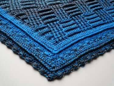 Gefaltetes gehäkeltes Dreieckstuch in Blau- und Grautönen mit Glitzergarn und verschiedenen Häkelmustern.