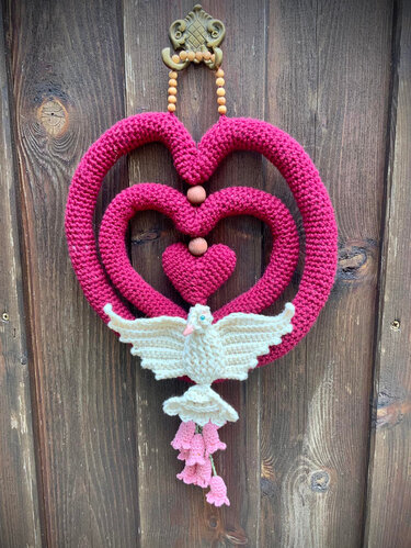 Gehäkelter Türkranz aus drei pinken Herzen mit Holzperlen, unten eine weiße Taube und rosa Blüten vor einer Holztür