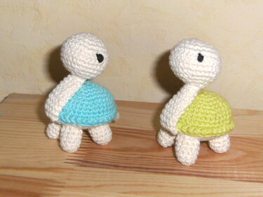 Zwei kompakte Amigurumi-Schildkröten mit blauem und grünem Panzer auf Holzuntergrund