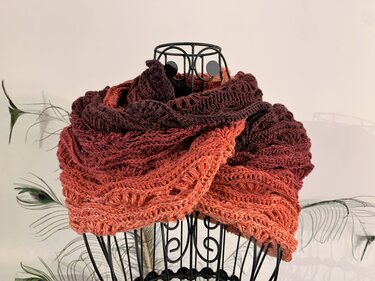 Ombre crochet cowl scarf in burgundy to coral on a black wire mannequin, showing textured stitch detail.