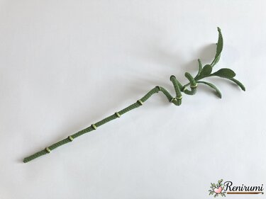 Long segmented crocheted stem with lighter ring accents and a cluster of leaves on a white surface