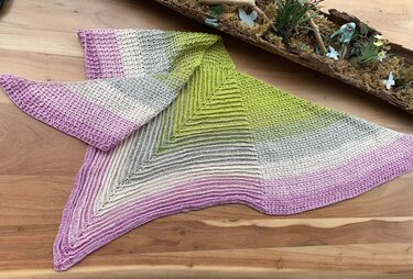 Gehäkeltes Dreieckstuch mit Farbverlauf in Lila, Beige, Grau und Limettengrün, ausgebreitet auf einer Holzoberfläche.