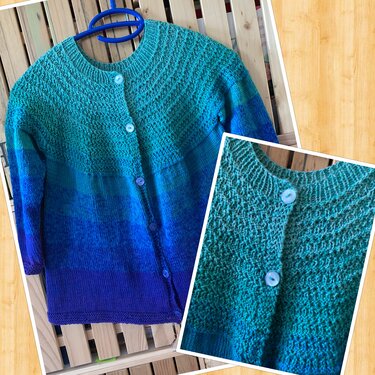 Gestrickte Kinderjacke in Türkis und Blau mit Farbverlauf und hellblauen Knöpfen an einem Kleiderbügel