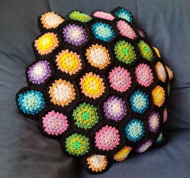 Kissenhülle aus zahlreichen gehäkelten Hexagon-Motiven mit bunten Mitteln und schwarzer Verbindung