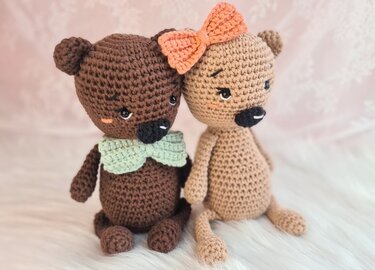 Zwei sitzende gehäkelte Amigurumi-Teddys, braun mit mintgrüner Fliege und beige mit korallfarbener Schleife
