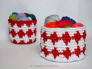 Zwei gehäkelte rot-weiße Körbe mit geometrischem Muster, gefüllt mit bunten Wollknäueln auf weißem Hintergrund
