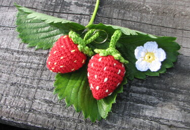 Zwei kleine gehäkelte Erdbeeren mit weißen Samenstichen und grünen Stielen auf Blättern