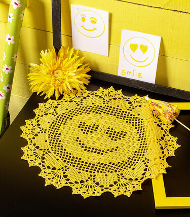 Rundes gelbes Häkeldeckchen mit Smiley auf dunklem Tisch