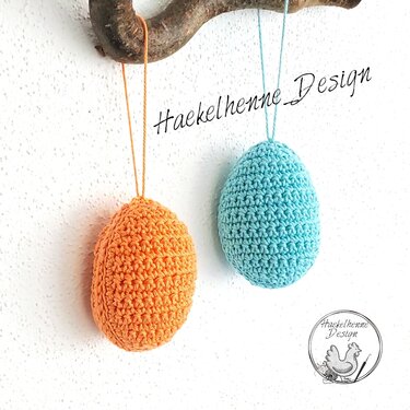 Zwei gehäkelte Ostereier in Orange und Türkis an einem Ast hängend