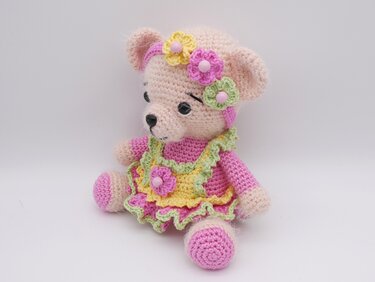 Sitzender, gehäkelter Amigurumi-Teddy in Pastellfarben mit Kleid, Volant und Blumen-Stirnband