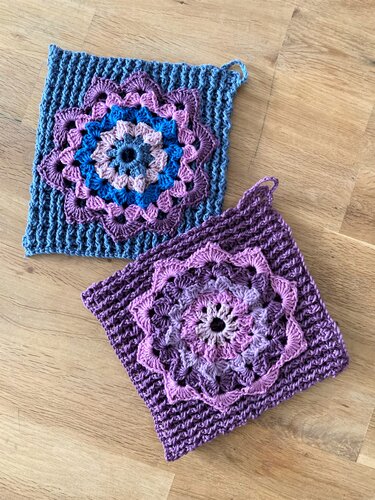 Zwei quadratische gehäkelte Topflappen mit Mandala-Motiv in Blau und Lila auf Holzboden.