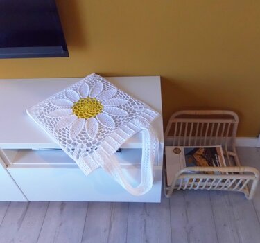 White crochet shopper bag with large daisy motif and yellow center draped over a white cabinet