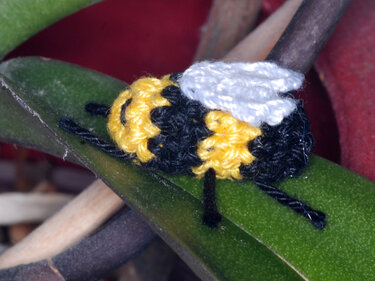 Gehäkelte Amigurumi-Biene mit gelb-schwarzen Streifen und weißen Flügeln auf grünem Blatt