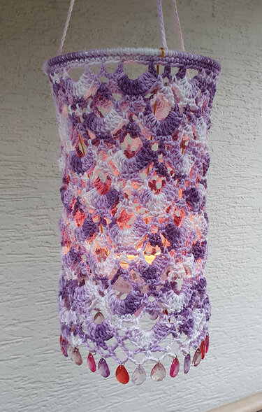 Zylindrische gehäkelte Laterne in Pastelllila und Rosa mit Muschelmuster und Perlenfransen, aufgehängt und beleuchtet
