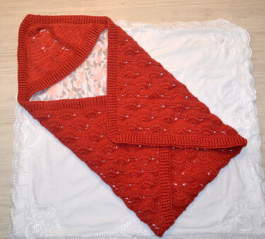 Gehäkelte Babydecke in Rostrot mit Kapuze und floralem Futter, gefaltet auf weißer Unterlage