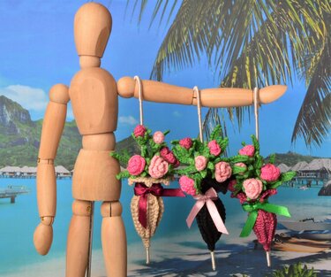 Wooden mannequin arm holding three crocheted hanging rose bouquets with pink flowers, green leaves and ribbon bows
