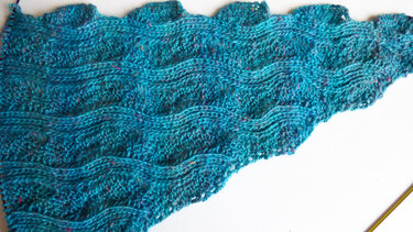 Detailansicht eines türkisfarbenen Dreieckstuchs mit Wellenmuster und sichtbarer Stricknadel am Rand