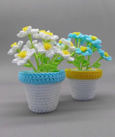 Farbenfrohe gehäkelte Blumen in kleinen weißen Töpfen mit farbigem Rand