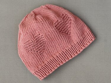 Einfach gestrickte rosa Babymütze mit Rippbündchen und Herzmuster