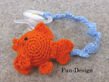 Orange gehäkelter Fisch als Schnullerhalter mit blauem Band und transparentem Befestigungsclip