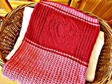 Gestrickte Babydecke rot-rosa mit Herzmuster im Weidenkorb