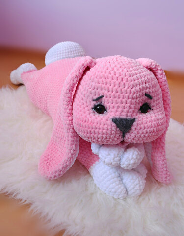 Rosa gehäkelter Amigurumi-Hase mit langen Ohren, weißen Pfoten und dunkler Nase