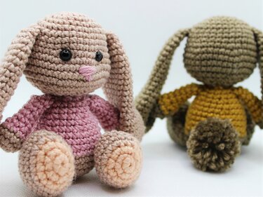 Zwei gehäkelte Amigurumi-Hasen, vorne rosa-beige und hinten gelb-braun, auf hellem Hintergrund.