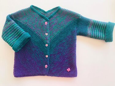Gestrickte Babyjacke türkis bis lila Farbverlauf mit rosa Herzknöpfen, umgeschlagenen Ärmeln und Schmetterlingsdetail, flach liegend