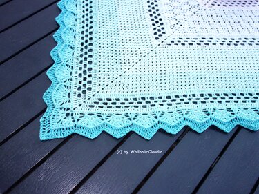 Eckdetail eines gehäkelten Tischläufers mit Weiß‑Türkis‑Verlauf und Muschelkante auf dunklem Holztisch