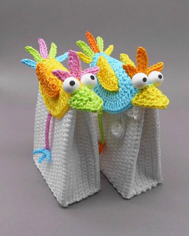 Three white crocheted rectangular bags topped with colorful crochet bird-head appliqués with large googly eyes