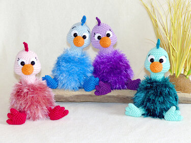 Vier bunte Amigurumi-Vögel mit flauschigem Gefieder in Rosa, Hellblau, Lila und Türkis
