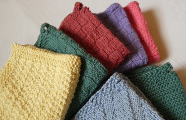 Fächerförmig angeordnete gestrickte Spültücher in Gelb, Grün, Blau, Rot und Lila mit verschiedenen Mustern