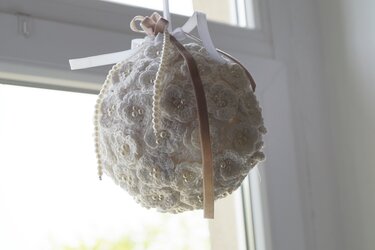 Weiße gehäkelte Kugel mit kleinen Blütenapplikationen und Perlen, aufgehängt an Bändern.