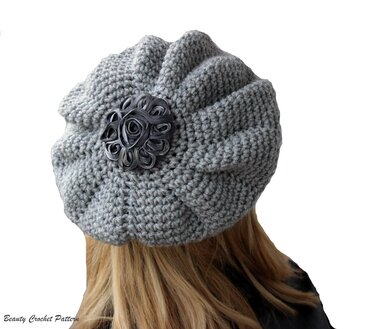 Back view of a light grey crocheted slouchy beret with radial ridges and a dark rosette at the center, worn by a person with long hair.