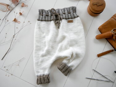 Weiß-graue gestrickte Babyhose mit grauem Rippenbund und Kordel flach gelegt