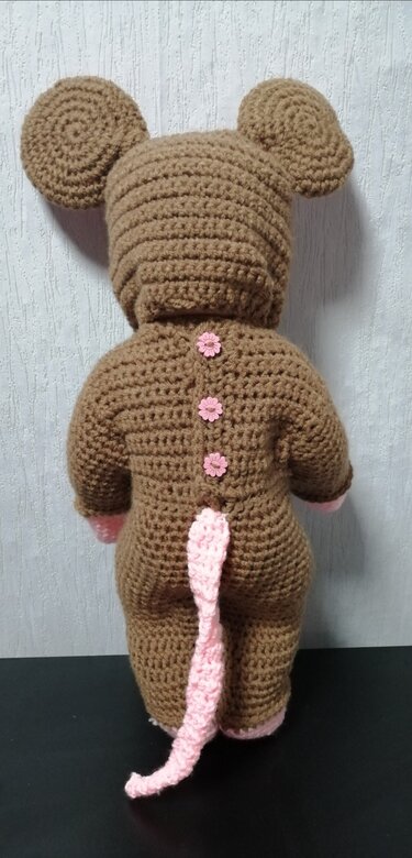 Rückansicht eines braunen, gehäkelten Maus-Kostüms mit Kapuze, runden Ohren, rosa Schwanz und rosa Blumenknöpfen.